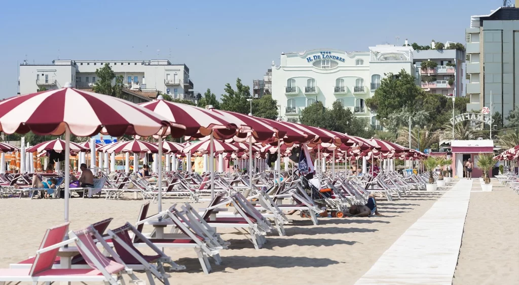 Spiaggia con file di ombrelloni rosso-bianco e lettini sotto un cielo sereno.